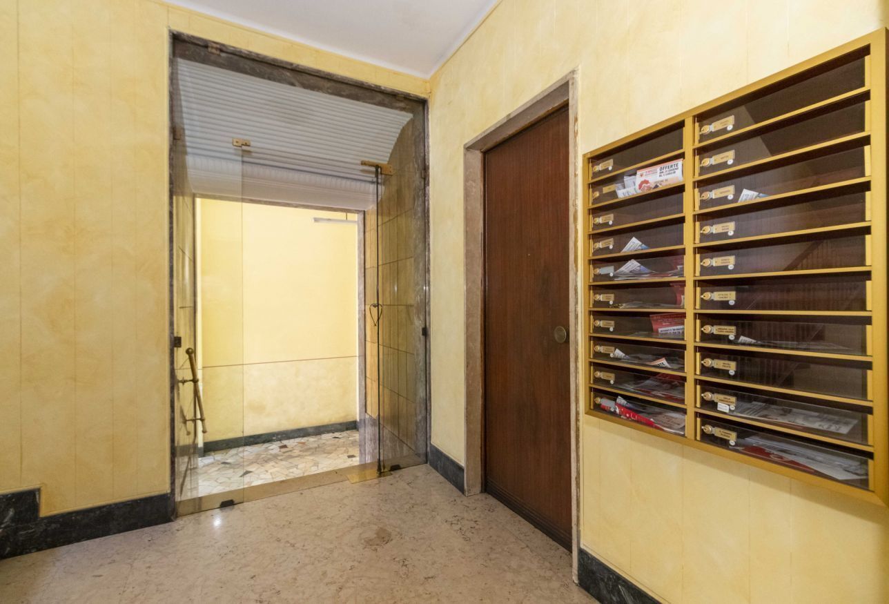 Un pasillo con una puerta cerrada, una puerta de cristal que da a una habitación y un mueble con buzones.