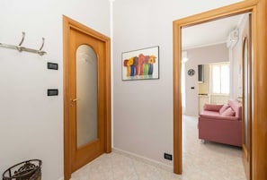 A hallway with a wooden door, a wall-mounted light switch, a framed picture of flowers, and a pink sofa in the background. - GuestHost - Santa Rita Neighborhood! Comfortable Appt x3 (Torino)