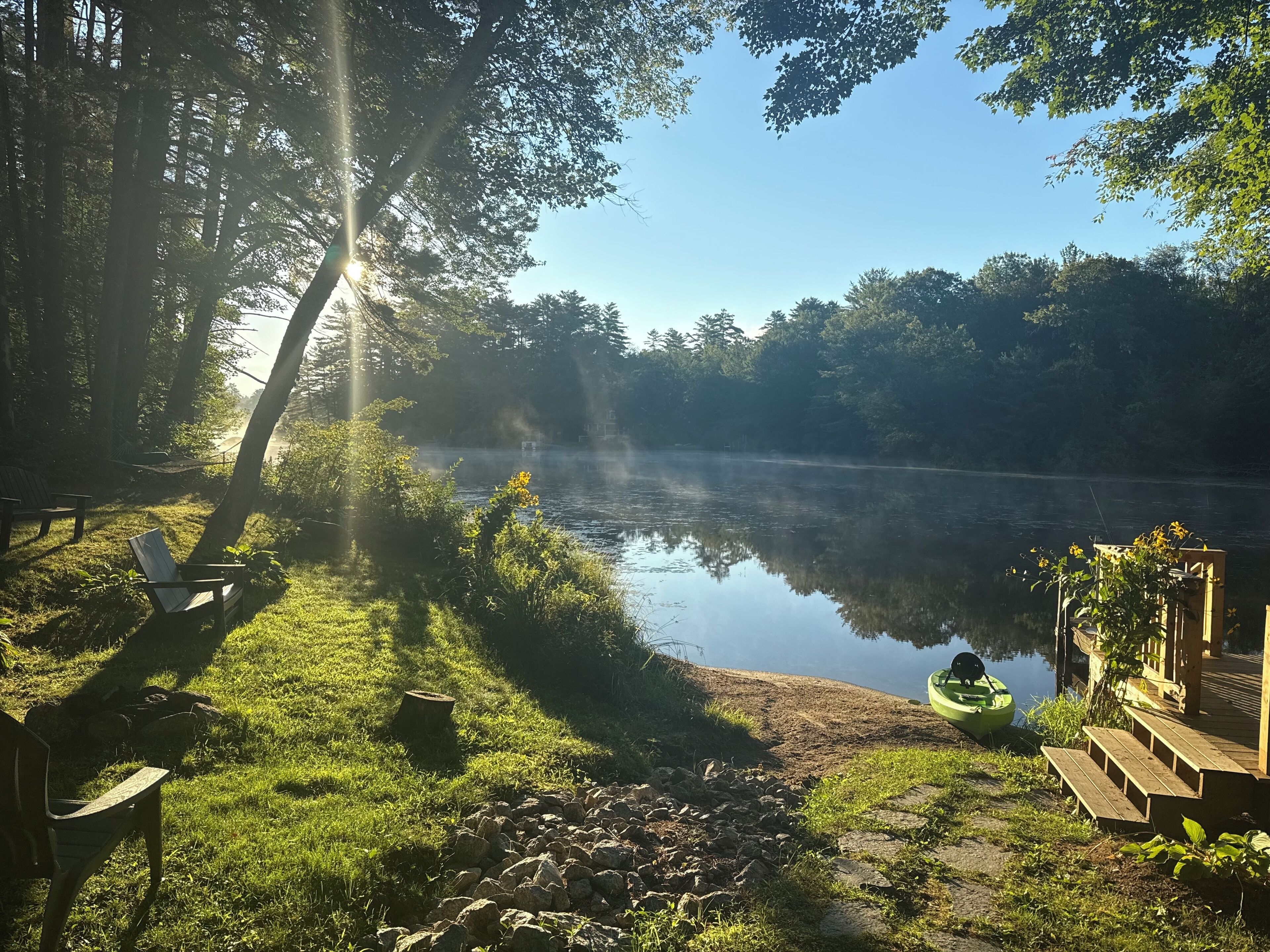 A serene lakeside setting with a wooden deck, a green kayak, and a hammock.