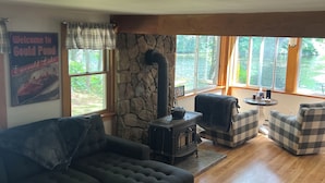 A cozy living room with a stone wall, a black wood-burning stove, a large sectional sofa, and plaid-patterned armchairs. - Cozy Lakeside Year Round Retreat ☀️🛶 🎣 🏊 🍁 🎃 🍎 🎿🏂 ❄️  & 🐾 are welcome 😊 (Hillsboro)