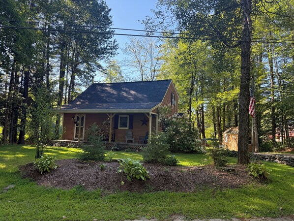A two-story house with a porch, surrounded by a forested area.