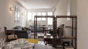 Ein geräumiges Wohnzimmer mit hohen Decken, einem Holztisch, einer Couch und einem Bücherregal.