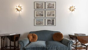 Ein Zimmer mit einem blauen Sofa, zwei Wandscheinwerfern und einer Reihe gerahmter Bilder an der Wand.