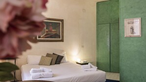 Hotellihuone, jossa on sänky, tyynyjä, yöpöytä, seinällä oleva kehystetty kuva ja yksi seinä, joka on maalattu korostevärillä.
