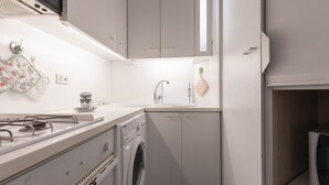 Pieni, käytännöllinen keittiö, jossa on liesi, pesukone ja kaapistot.