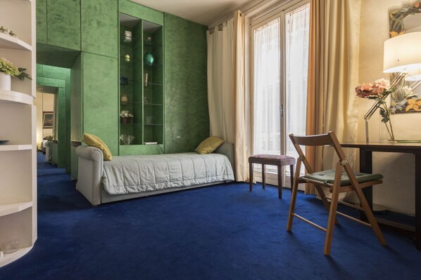 A room with a green accent wall, a bed, a desk with a chair, and a window with curtains. - Ponte vecchio Living (Firenze)