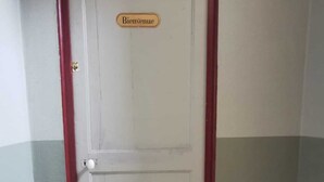 Uma porta com a placa 'Bienvenue' acima, um tapete de entrada com 'Bienvenue' e um símbolo de chave, e um chão estampado.