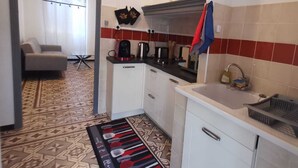 Cozinha compacta com armários brancos, painel de azulejos vermelho e bege, cafeteira e pia.