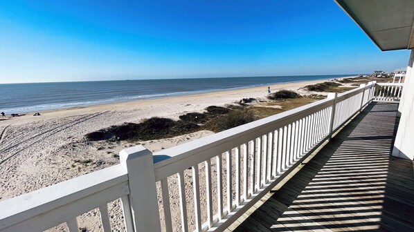 Vista a la playa desde un balcón con terraza de madera y barandilla blanca.