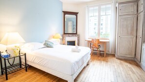 Quarto de hotel com cama, mesa de cabeceira com abajur, escrivaninha com cadeira, espelho grande e guarda-roupa.