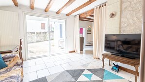 Uma sala de estar ampla com uma grande porta de vidro deslizante que dá para uma área externa, uma TV de tela plana em um suporte de madeira, e um tapete estampado no chão.
