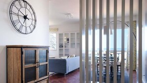Ein modernes Wohnzimmer mit einem Holzkabinett, einer großen Wanduhr und Blick durch eine Glastrennwand auf einen Essbereich im Freien.