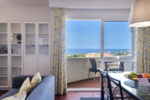 Une pièce comprenant un canapé, une table à manger avec des chaises, un meuble vitré et une vue sur la mer.