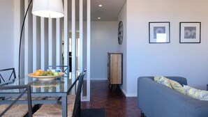 Ein modernes Wohnzimmer mit Essbereich, einer Couch, einem Tisch mit Obst und gerahmten Bildern an der Wand.