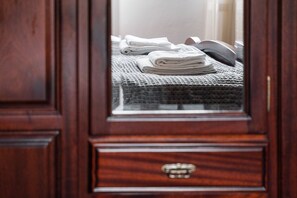 Puerta de madera con un espejo que refleja una cama bien hecha, con un edredón gris con textura y toallas blancas dobladas.