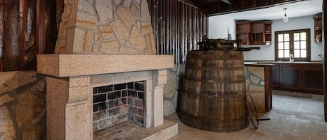 Un interior rústico con chimenea de piedra, un barril de madera y una zona de cocina con armarios de madera y un ventanal.