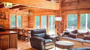 A spacious cabin interior with a high ceiling, wooden walls, a dining area, and a seating area with a sofa and chairs. - Log Cabin w/ Hot Tub - close to Whiteface (Wilmington)