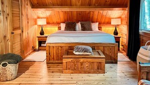 A wooden cabin bedroom with a bed, two nightstands, a wooden chest, and a window. - Log Cabin w/ Hot Tub - close to Whiteface (Wilmington)