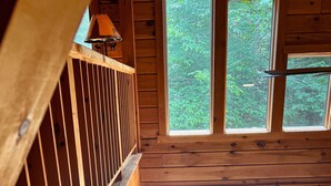 A cabin interior with a wooden deck, a sofa with cushions, and a table with a lamp. - Log Cabin w/ Hot Tub - close to Whiteface (Wilmington)