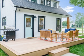 Een huis met een overdekte veranda, een barbecue en buiten zitplaatsen.