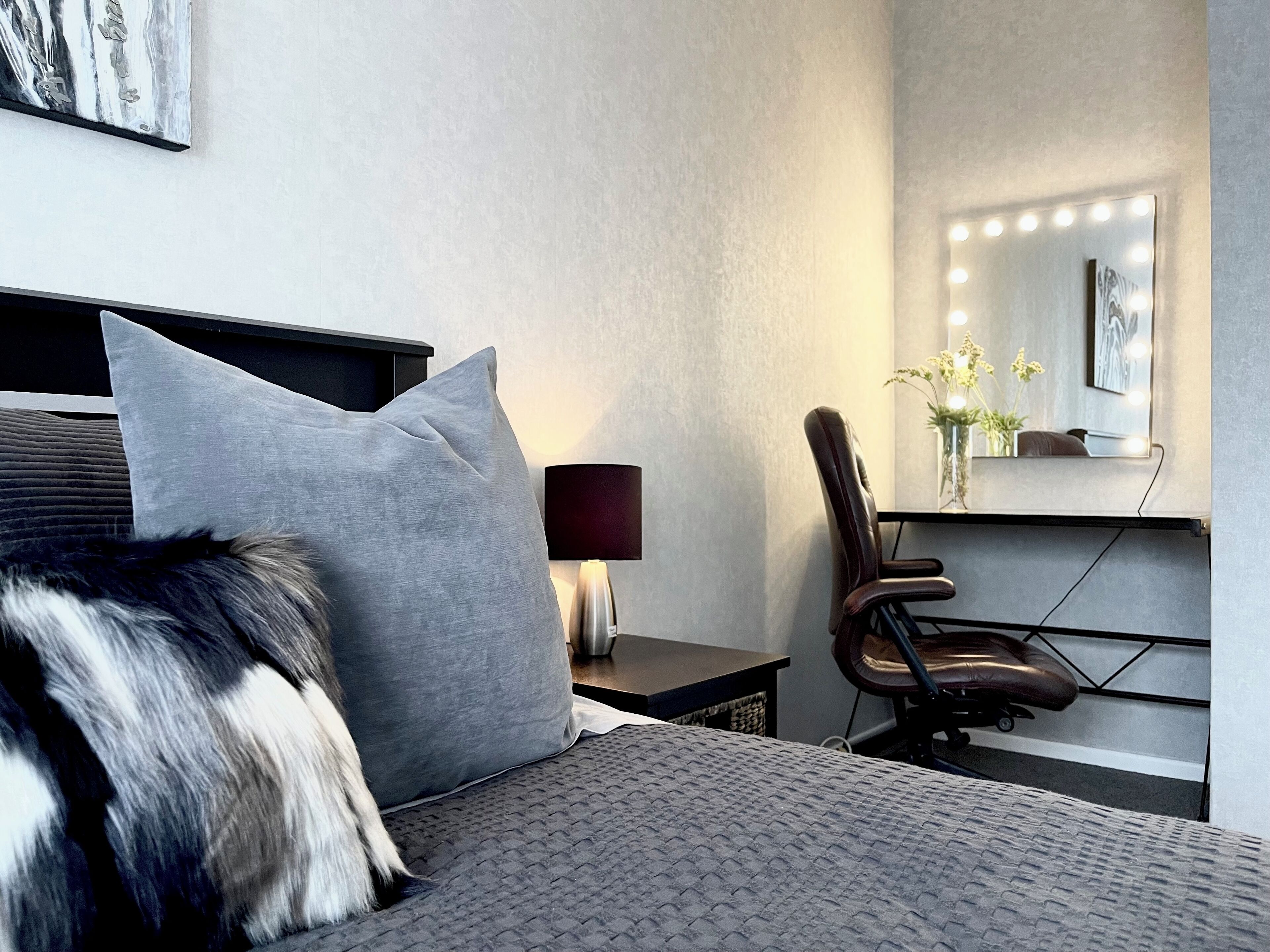 Moderni hotellihuone, jossa on sänky, työpöytä, tuoli, lamppu ja valaistu meikkipöytä.