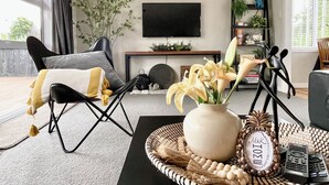Un salon moderne avec un canapé noir, une table basse ornée d’un vase de fleurs et un téléviseur fixé au mur.