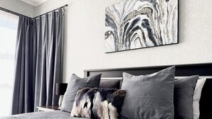 Une chambre à coucher moderne avec un grand lit, une literie grise et un plaid en fausse fourrure.