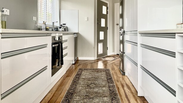 Une cuisine moderne avec des meubles blancs, une hotte en acier inoxydable et un plancher en bois.
