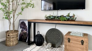 Un salon moderne avec un téléviseur à écran plat fixé au mur, une console en bois agrémentée de plantes décoratives, une œuvre d’art encadrée, une lanterne noire et un jeu d’échecs.