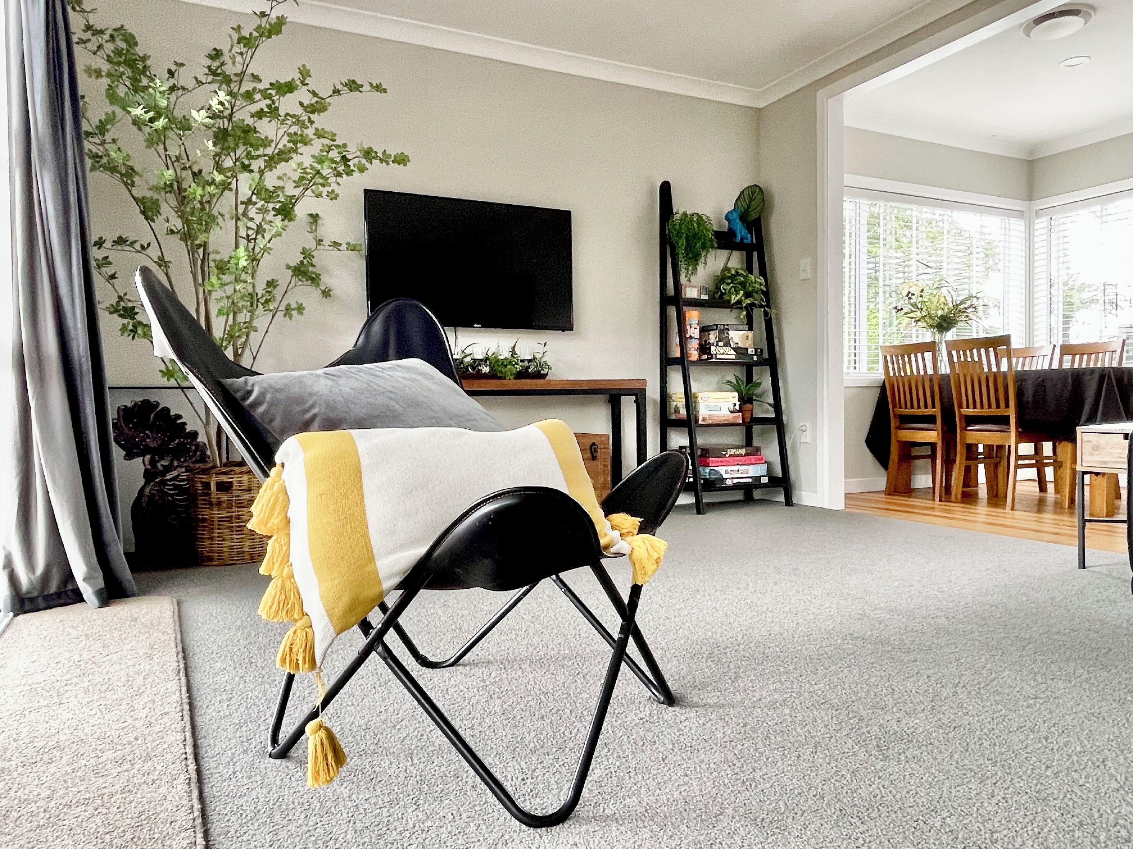 A living room with a black lounge chair, a flat-screen TV, a bookshelf, and a dining area with wooden chairs and a table.