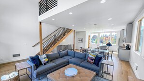 A spacious living area with a sectional sofa, a coffee table, and a staircase leading to an upper level. - New! Modern Ski-in/Ski-out Mountain View Chalet by Village + Hot Tub/EV Charging (Snoqualmie Pass)