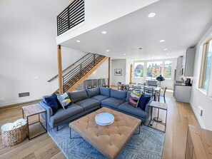 A spacious living area with a sectional sofa, a coffee table, and a staircase leading to an upper level. - New! Modern Ski-in/Ski-out Mountain View Chalet by Village + Hot Tub/EV Charging (Snoqualmie Pass)