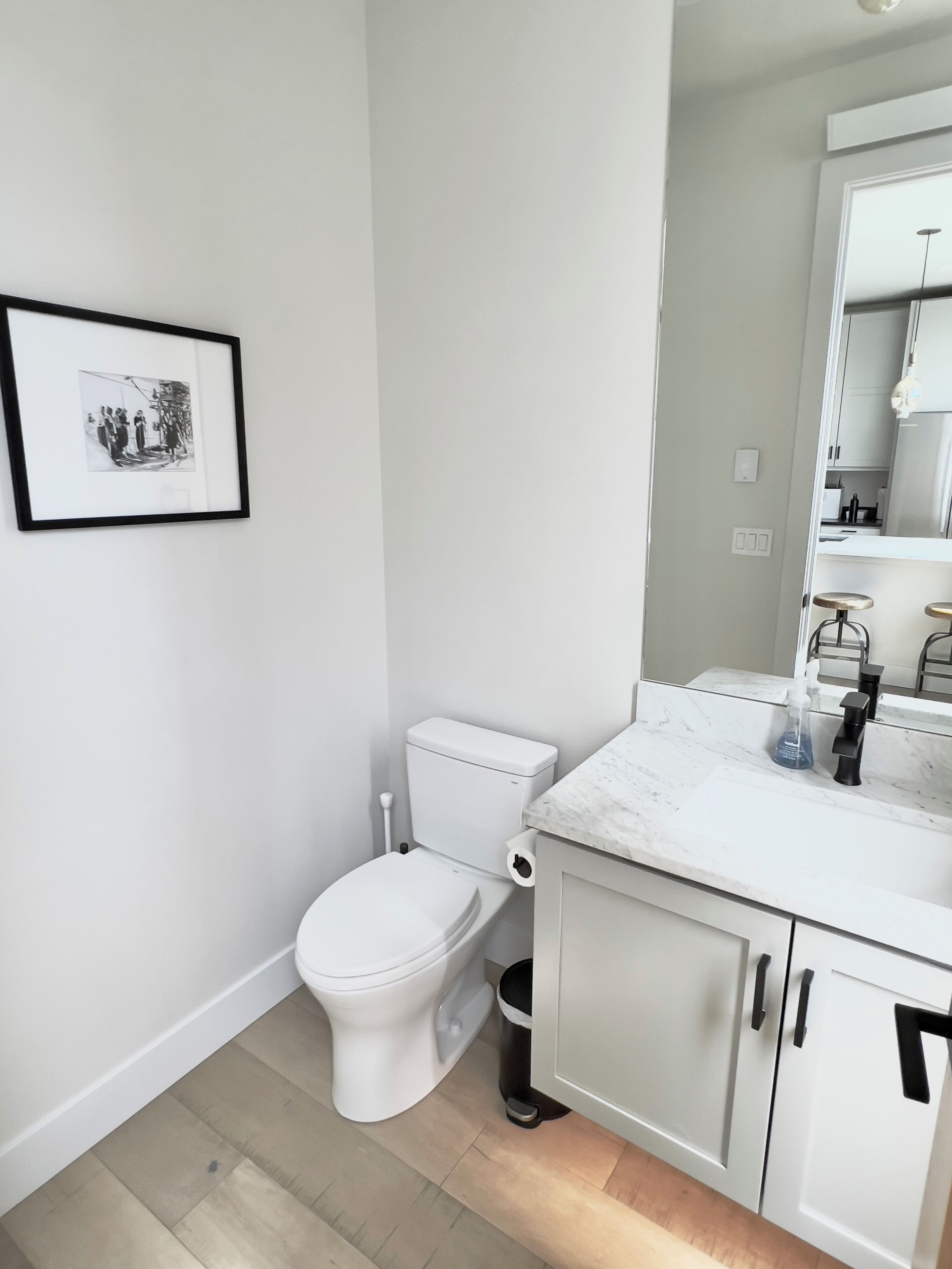Ein modernes Badezimmer mit einer weißen Toilette, einem мраморном Waschtisch und einem gerahmten Bild an der Wand.