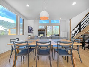 A modern dining area with a large wooden table and chairs, a fireplace, and a view of mountains through large windows. - New! Modern Ski-in/Ski-out Mountain View Chalet by Village + Hot Tub/EV Charging (Snoqualmie Pass)