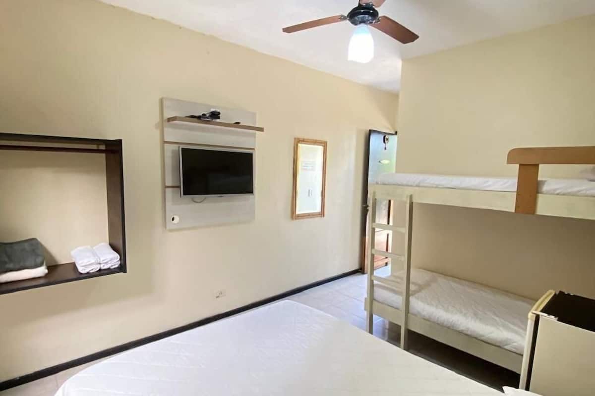 A hotel room with a large bed, a ceiling fan, a TV mounted on the wall, and a bunk bed.