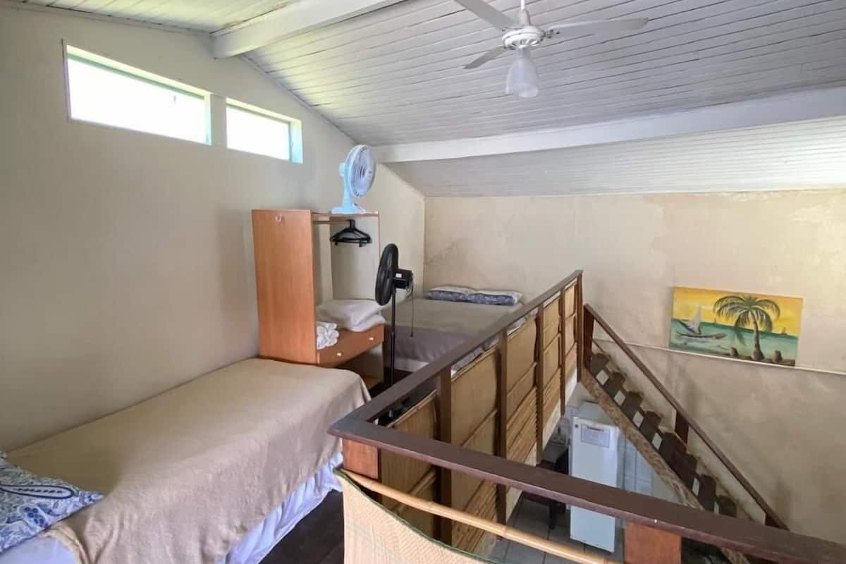 A compact room with a bunk bed, a desk with a chair, a ceiling fan, and a small window.