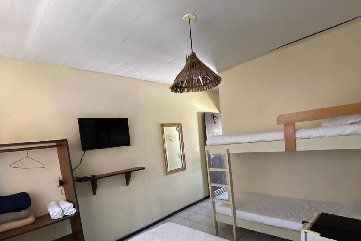 A hotel room with a single bed, a bunk bed, a TV, a mirror, and a hanging light fixture.
