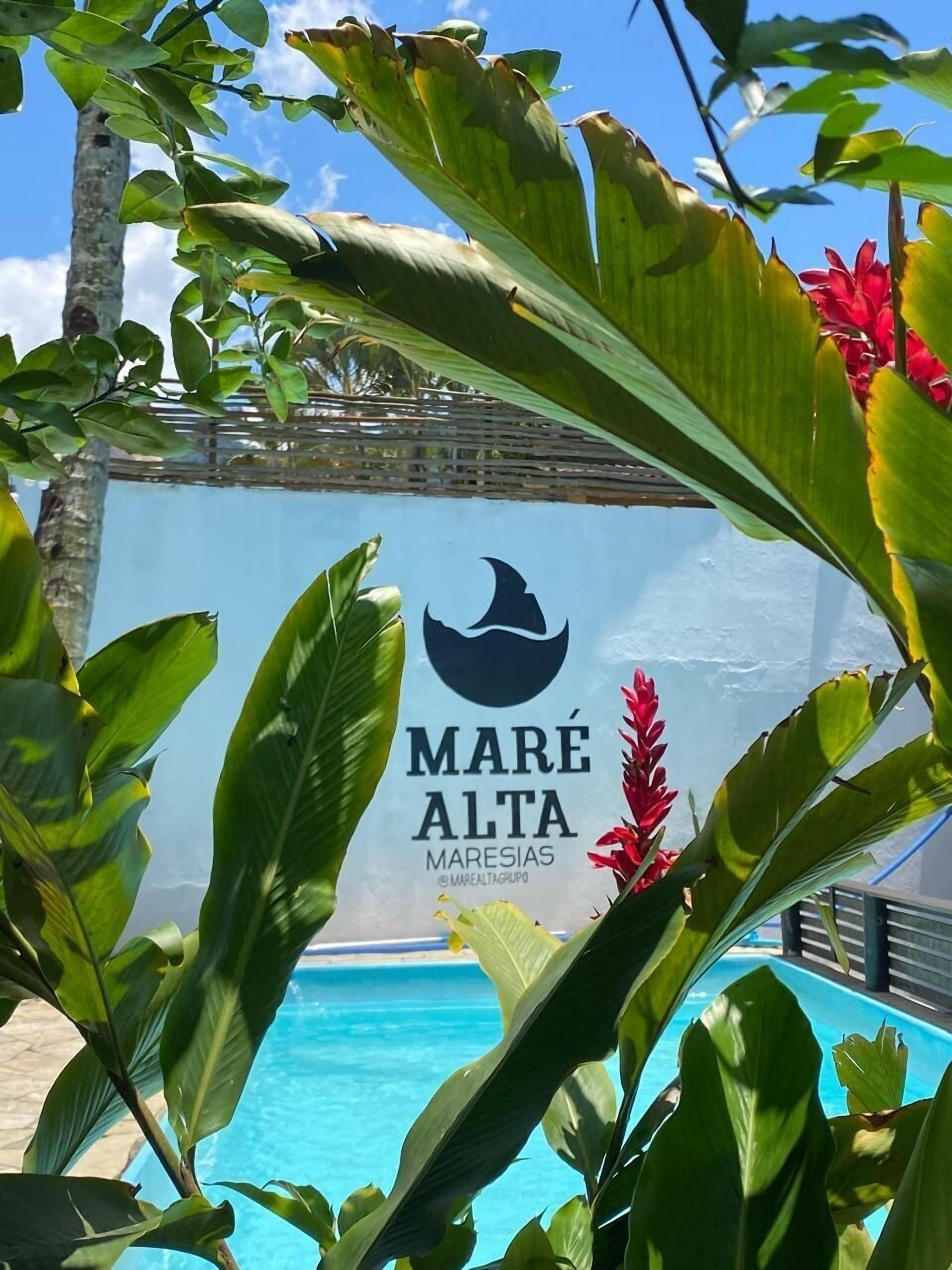 Zona de piscina con un letrero que dice "MARE ALTA MARESIAS" y plantas tropicales.