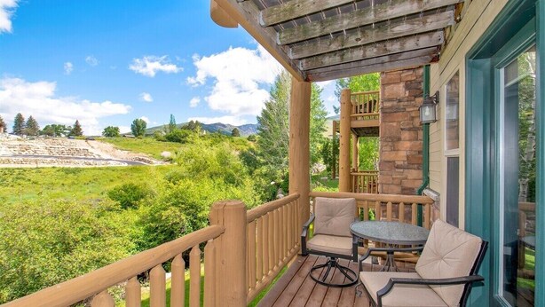 Une terrasse en bois avec une table et des chaises, offrant une vue sur un paysage verdoyant et luxuriant ainsi que sur des montagnes.
