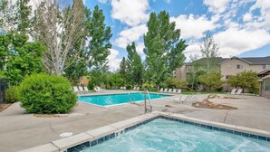 Une piscine dotée de chaises longues et d’un petit jacuzzi, le tout entouré d’arbres et d’immeubles.