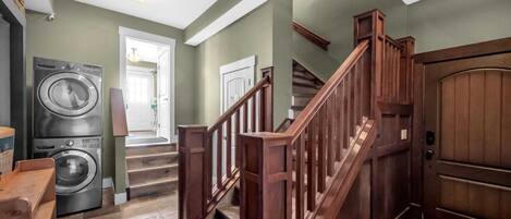 A laundry room with a washing machine, a dryer, and a wooden staircase leading to a door.