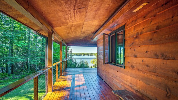Une cabane en bois dotée d’une terrasse offrant une vue sur une forêt et un lac.