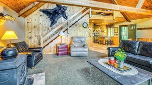 Un salon chaleureux avec une cheminée, des canapés en cuir, un escalier en bois et une cuisine en arrière-plan.
