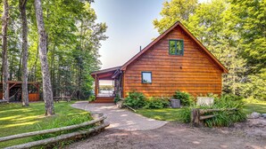 Une cabane en bois dotée d’un porche, entourée d’arbres et bordée d’un chemin de gravier.