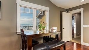 A dining area with a view of a cityscape through a large window, a wooden dining table, and a bench. - Rocky View Bed and Breakfast Garden Room (Calgary)