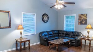 A living room with a black leather sectional sofa, a wooden coffee table, two side tables with lamps, a ceiling fan, and a clock on the wall. - Cheerful 3-Bed Room Home in Columbus, MS  (Columbus)