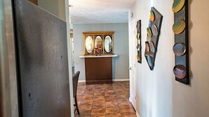 A hallway with a tiled floor, a wooden cabinet with two mirrors, and a wall with abstract art. - Cheerful 3-Bed Room Home in Columbus, MS  (Columbus)