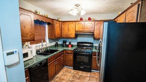 A compact kitchen with wooden cabinets, a black refrigerator, a stove, and a microwave. - Cheerful 3-Bed Room Home in Columbus, MS  (Columbus)