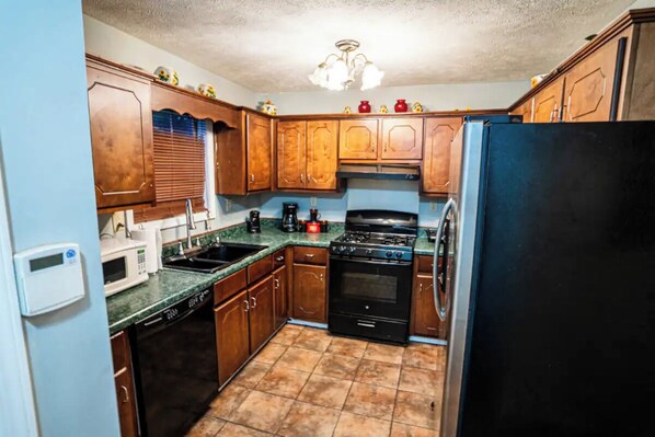 A compact kitchen with wooden cabinets, a black refrigerator, a stove, and a microwave. - Cheerful 3-Bed Room Home in Columbus, MS (Columbus)