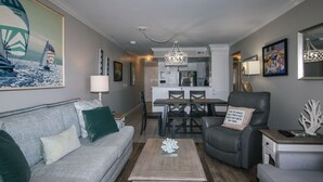 A living room with a grey sofa, a coffee table, and a dining area with a table and chairs. - 216 Bay Creek Villa-Beautiful 2nd Floor Villa;Private Balcony;Water Views;Communal Pool (Edisto Beach)